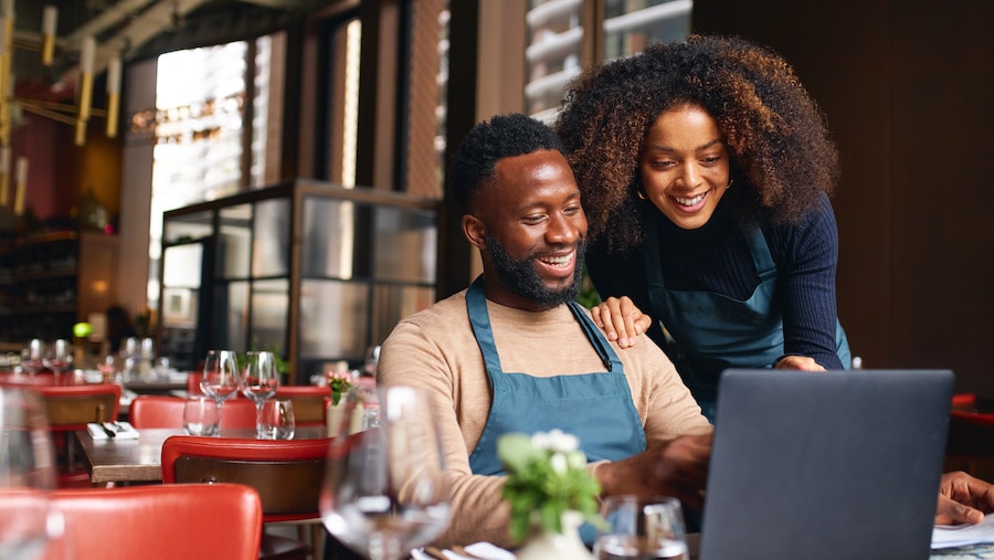Black business owners smiling and looking at their laptop.