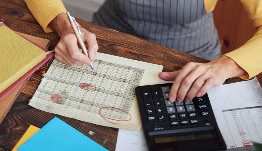 Person sitting down and making some calculations using a calculator and data sheet.
