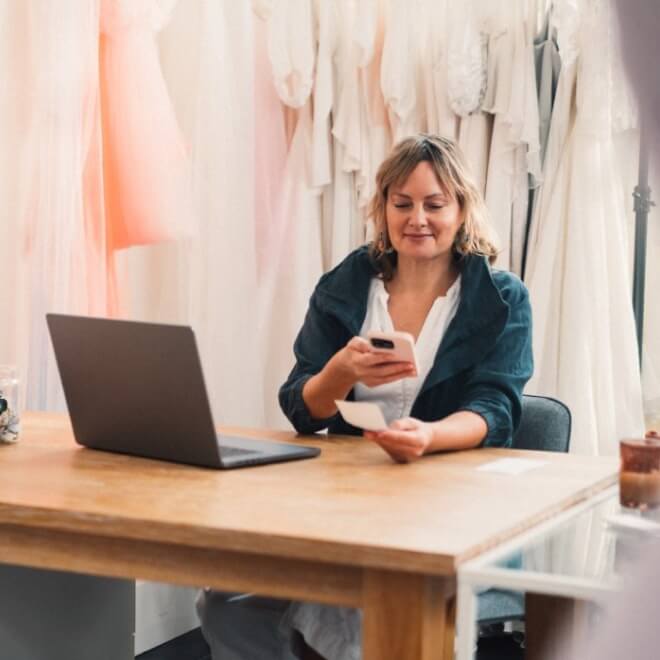Bridal shop owner at desk, scanning a paper receipt to upload with her smartphone app 