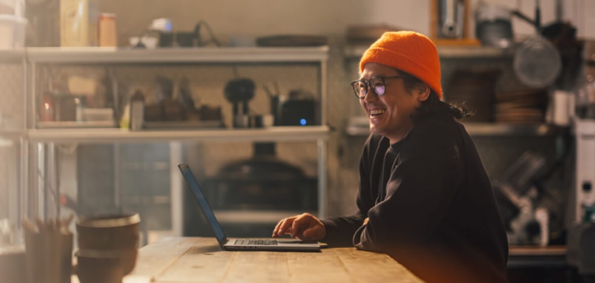 Business owner in their restaurant, smiling and working at their laptop.