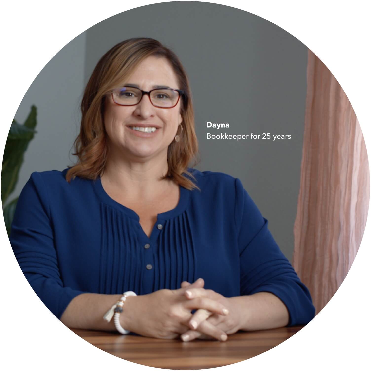 A bookkeeper sitting at a desk smiling into camera.