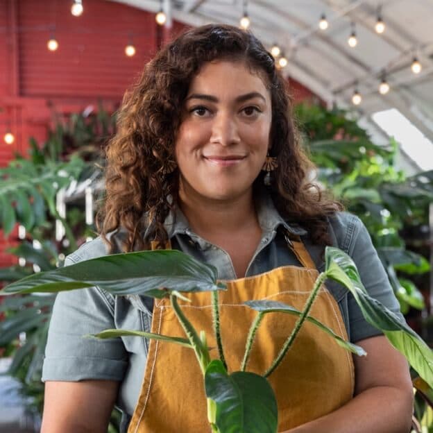 Photo of a person smiling at the camera while holding a plant in their hands.