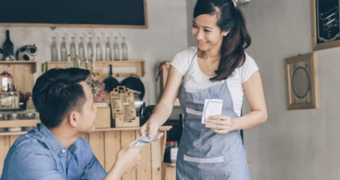 Coffee shop owner taking a cash payment from a customer.