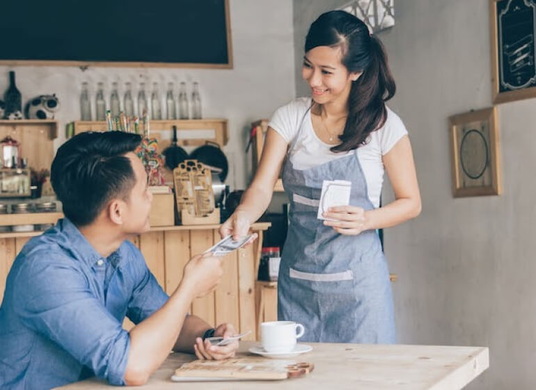 Coffee shop owner taking a cash payment from a customer.