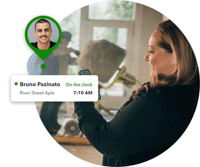 A business owner looking at her phone while an employee works in the background and an overlay image of the employee's profile image and time clocked in.